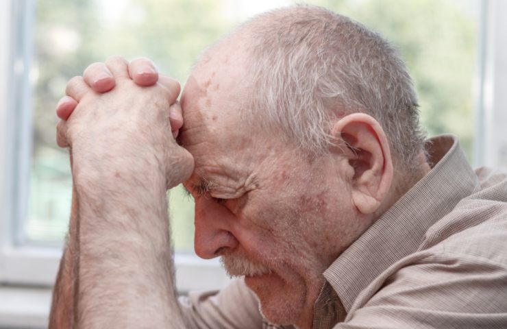 uomo anziano con le mani congiunte e l'espressione triste