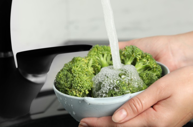 donna che sciacqua i broccoli sotto l'acqua