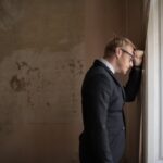 uomo disperato con la fronte appoggiata alla parete