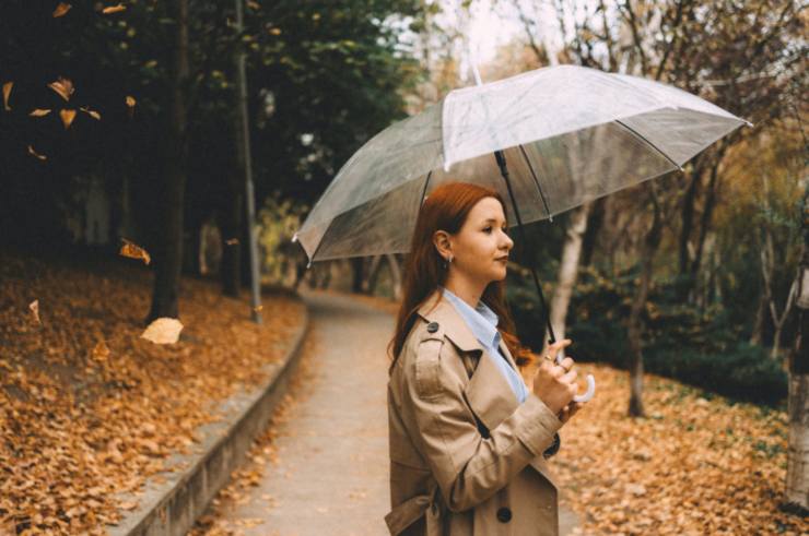 donna in un bosco con un trench beige e un ombrello aperto