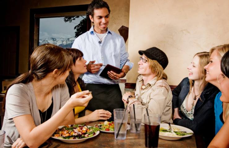 tavolo di persone che parlano con un giovane cameriere al ristorante