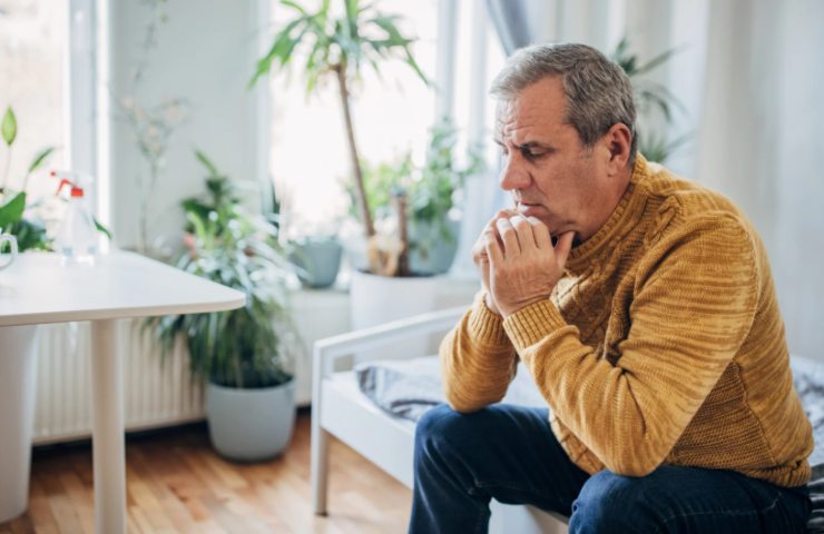 uomo seduto sul divano con espressione preoccupata e le mani sotto al mento