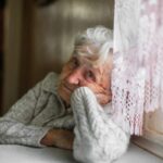 donna anziana triste seduta al tavolo vicino alla finestra