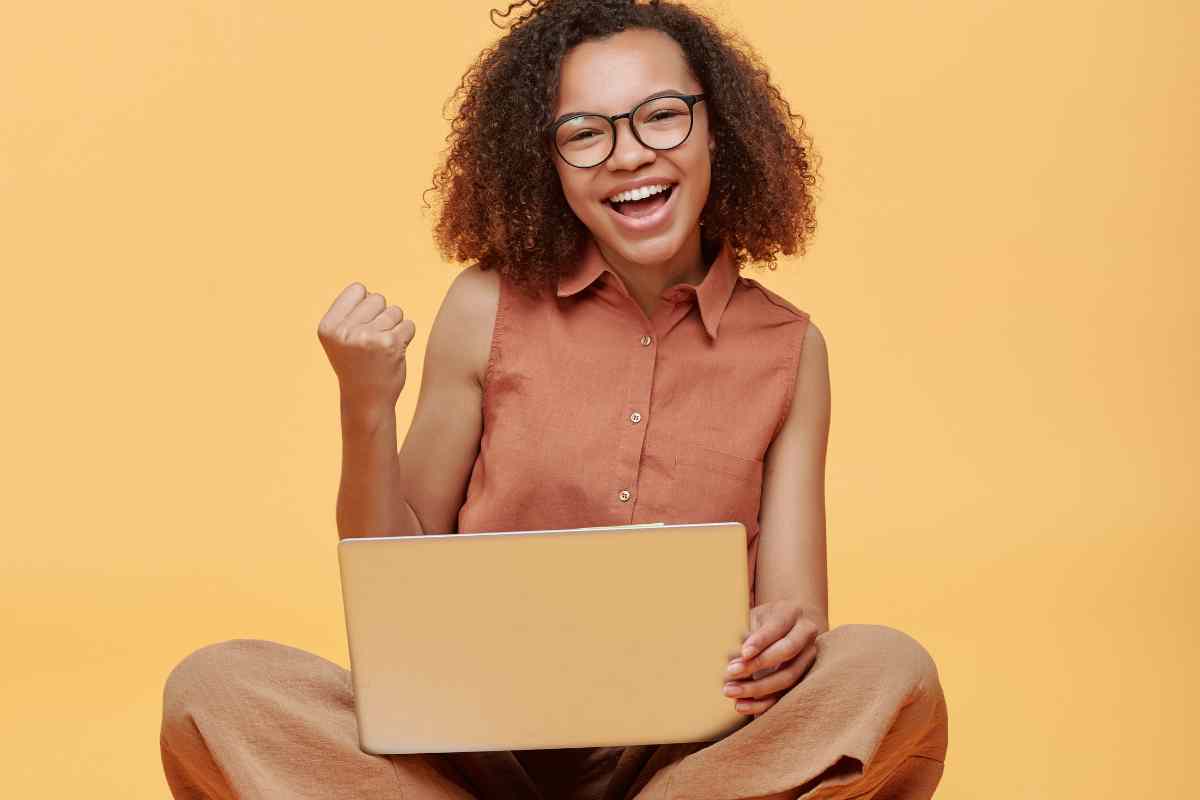 ragazza felice con il pc portatile fra le gambe incrociate partecipa al corso online WordPress gratis