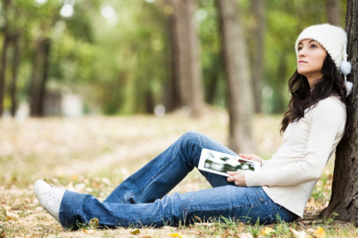 donna in un bosco seduta ai piedi di un albero