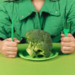 donna con forchetta e coltello e davanti a lei un piatto con sopra un broccolo crudo