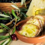 fette di pane con sopra dell'olio e accanto un ramo di ulivo e delle olive
