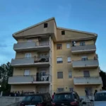 Condominio a tre piani visto dall'esterno con auto parcheggiate davanti.