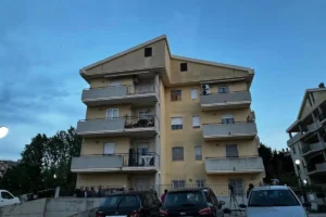 Condominio a tre piani visto dall'esterno con auto parcheggiate davanti.
